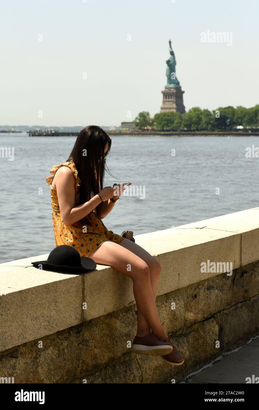New York, USA - June 09, 2018: The girl use a smartphone at the Ellis Island with  the Statue of Liberty on the background. Stock Photo
