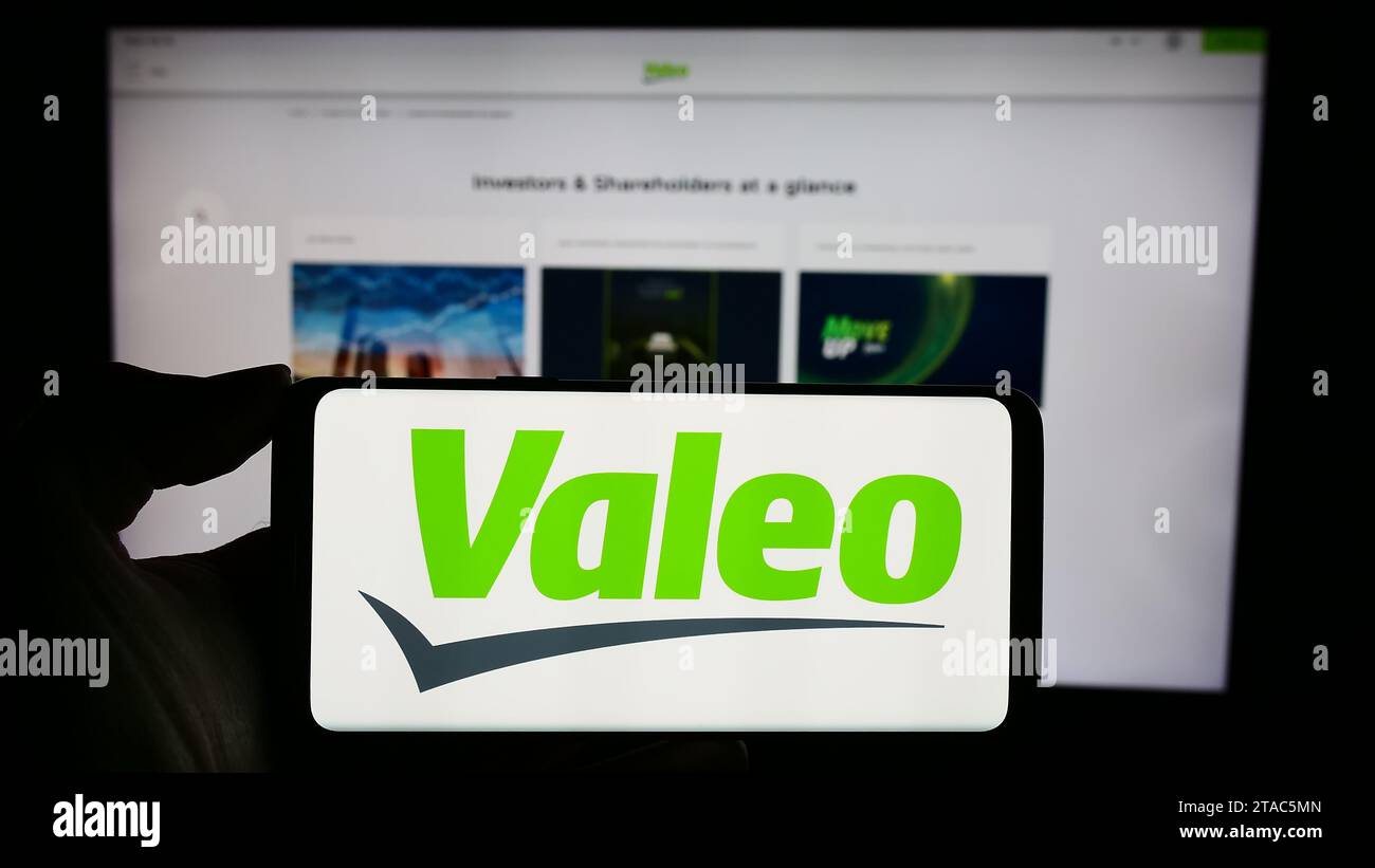 Person holding cellphone with logo of French automotive supply company Valeo S.A. in front of business webpage. Focus on phone display. Stock Photo