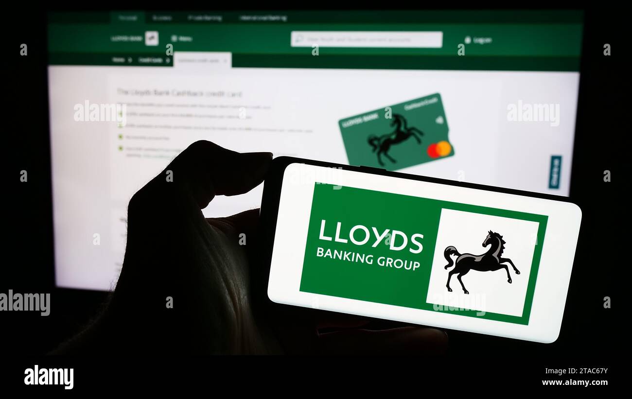 Person holding cellphone with logo of British financial company Lloyds Banking Group plc in front of business webpage. Focus on phone display. Stock Photo