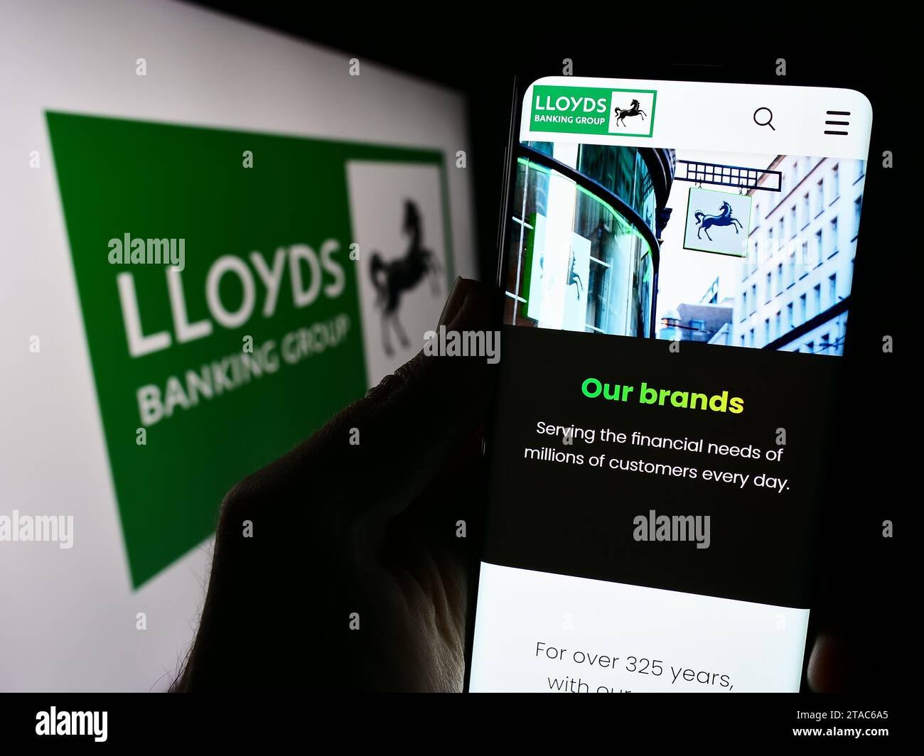 Person holding smartphone with webpage of British financial company Lloyds Banking Group plc in front of logo. Focus on center of phone display. Stock Photo