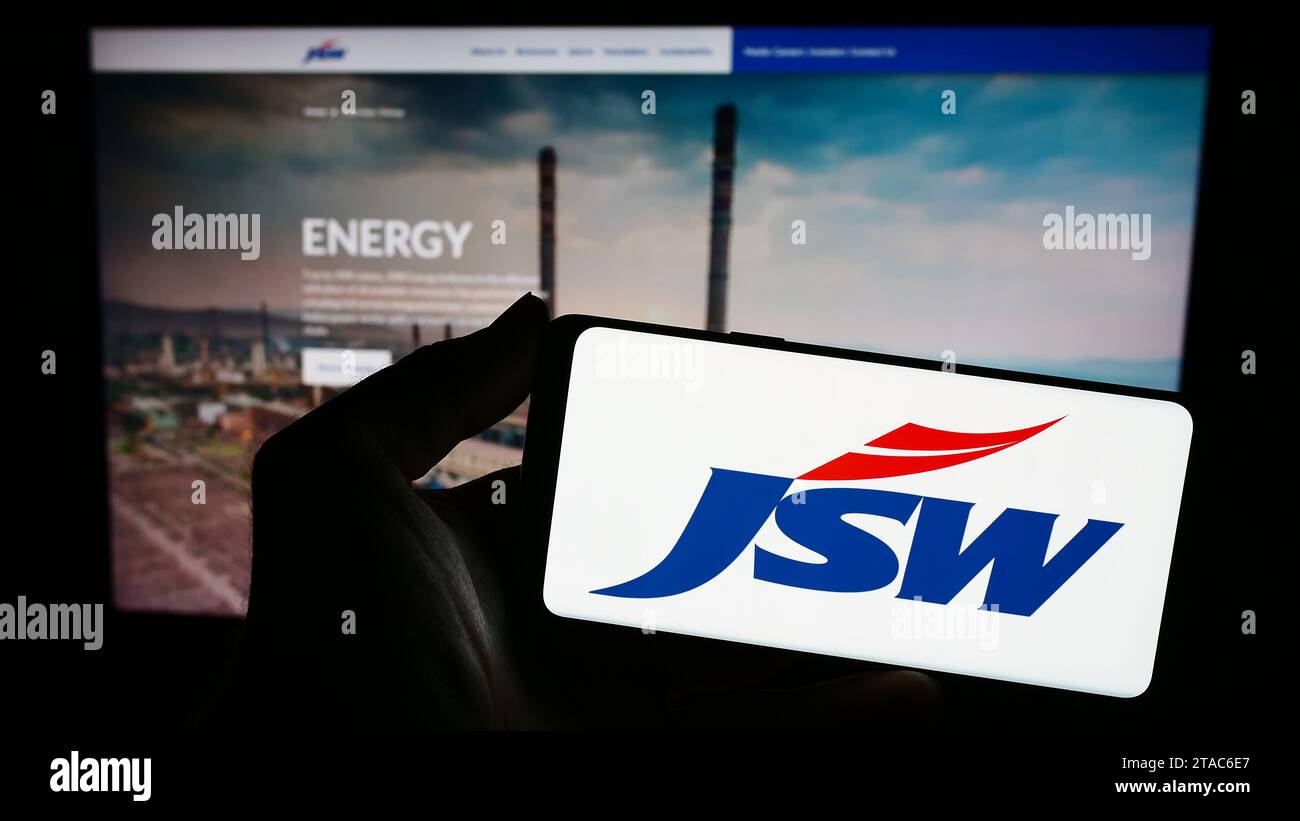 Person holding smartphone with logo of Indian conglomerate JSW Group in front of website. Focus on phone display. Stock Photo