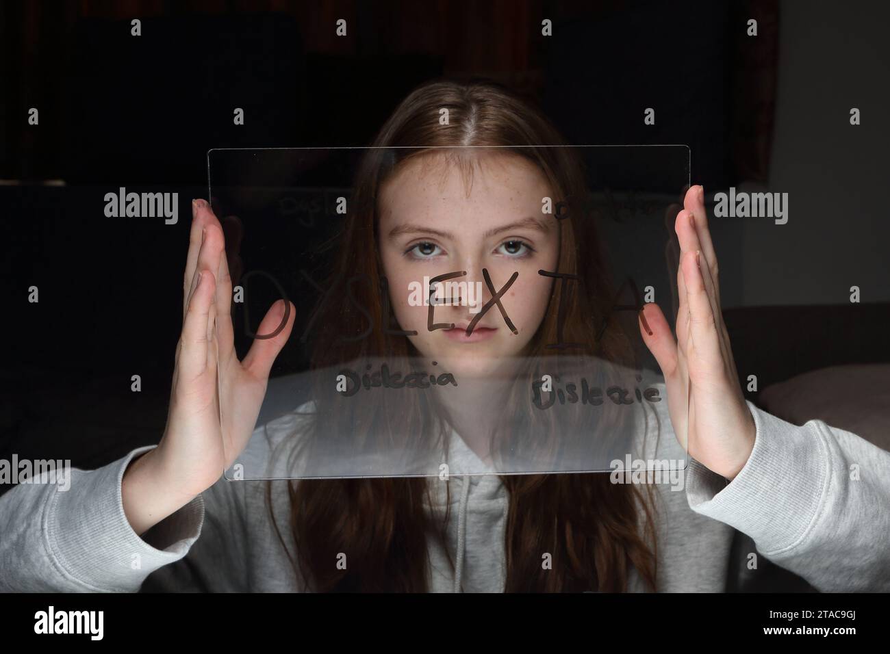Teenage girl holds transparent plastic board with words related to dyslexia in front of her face, including misspellings Stock Photo
