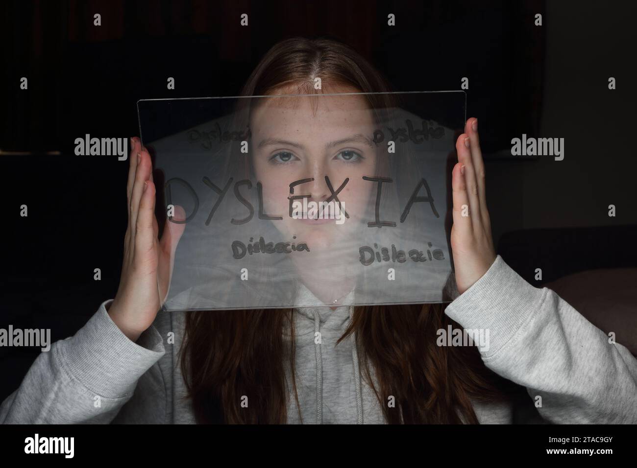 Teenage girl holds transparent plastic board with words related to dyslexia in front of her face, including misspellings Stock Photo