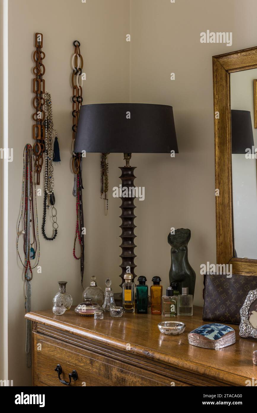 Lamp and perfume with necklaces on dressing table in colonial style single-storey home. Truro, Cornwall, UK. Stock Photo