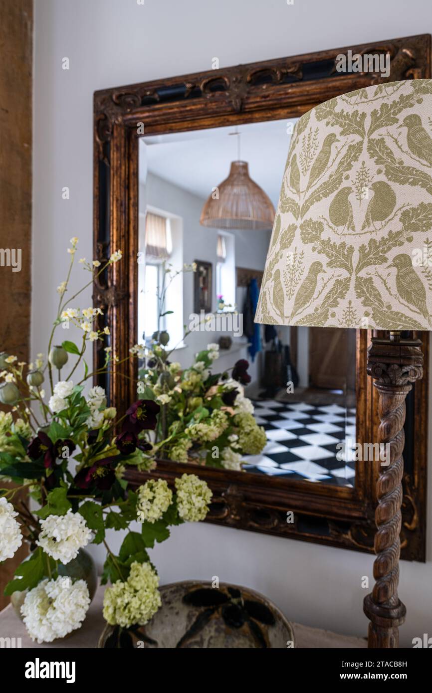 Lampshade and cut flowers with 1930s Arts and Crafts style entrance hall reflected in mirror. Hove, East Sussex, UK. Stock Photo