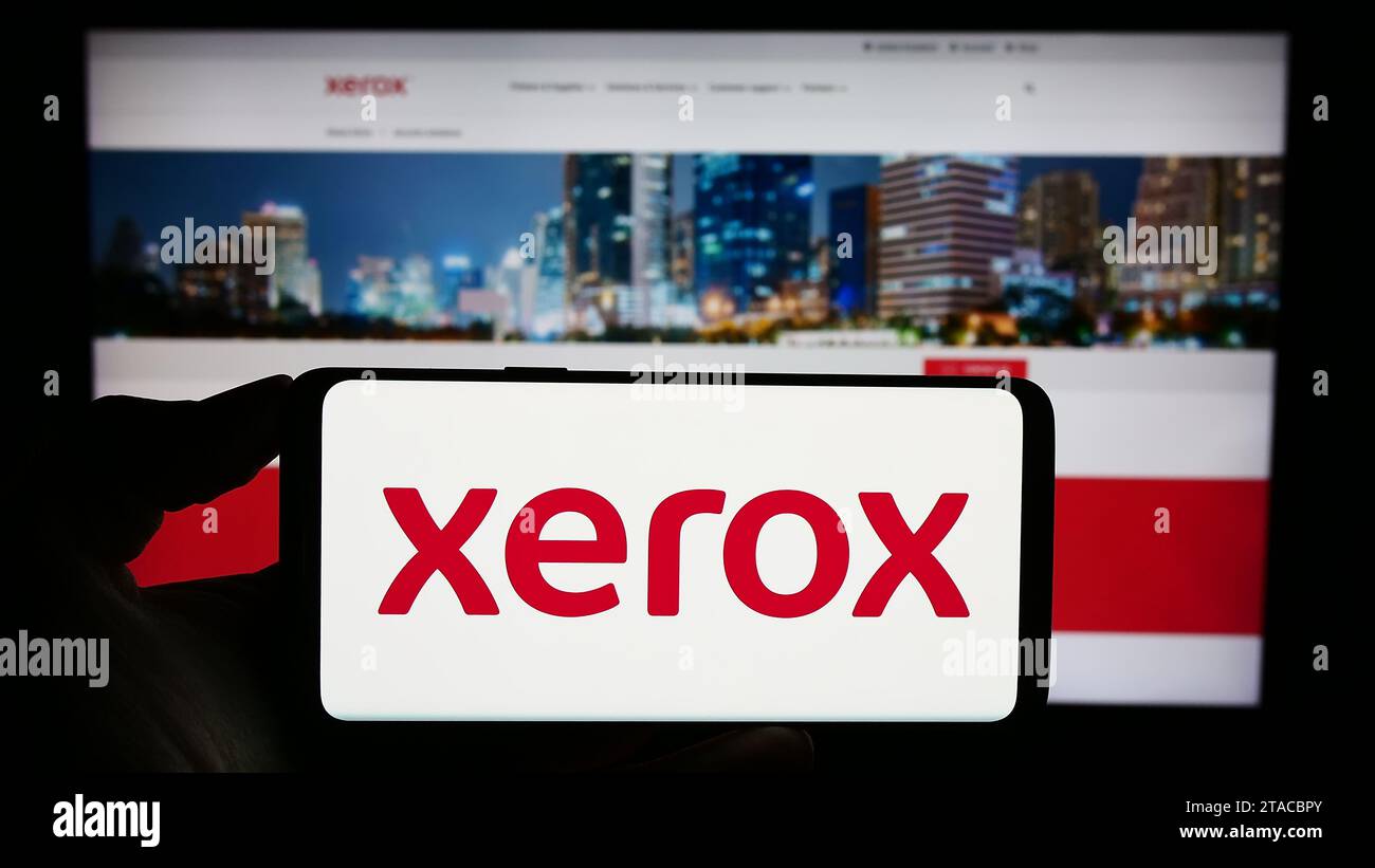 Person holding cellphone with logo of US printer company Xerox Holdings Corporation in front of business webpage. Focus on phone display. Stock Photo