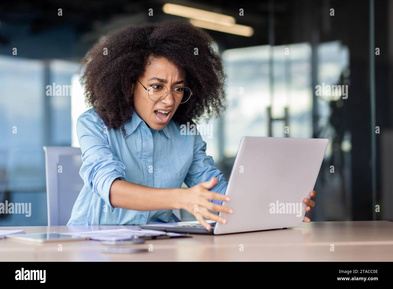 Woman at the workplace inside the office is not satisfied with the work of the computer, a frustrated businesswoman is shouting at a broken laptop, and overpriced broken software. Stock Photo