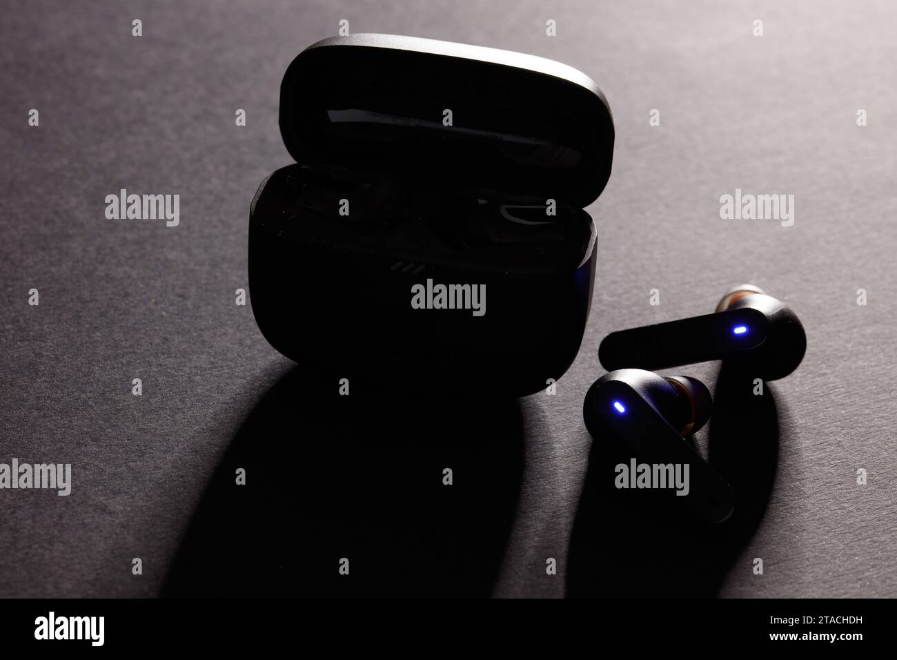 a studio shot of a pair of black jbl wireless bluetooth earphones, against a dramatically lit black background Stock Photo