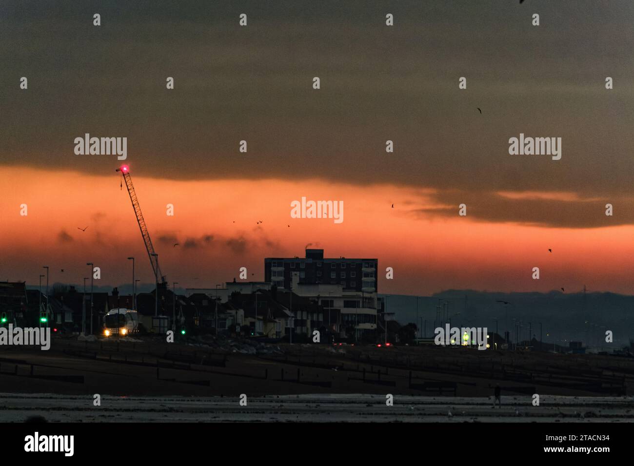 Commuters drive along East Worthing and Lancing seafront on a Cold November morning on Thursday 30 November 2023 as seen from Worthing Beach, Worthing. The sunrise creates a deep red sky overhead. Stock Photo