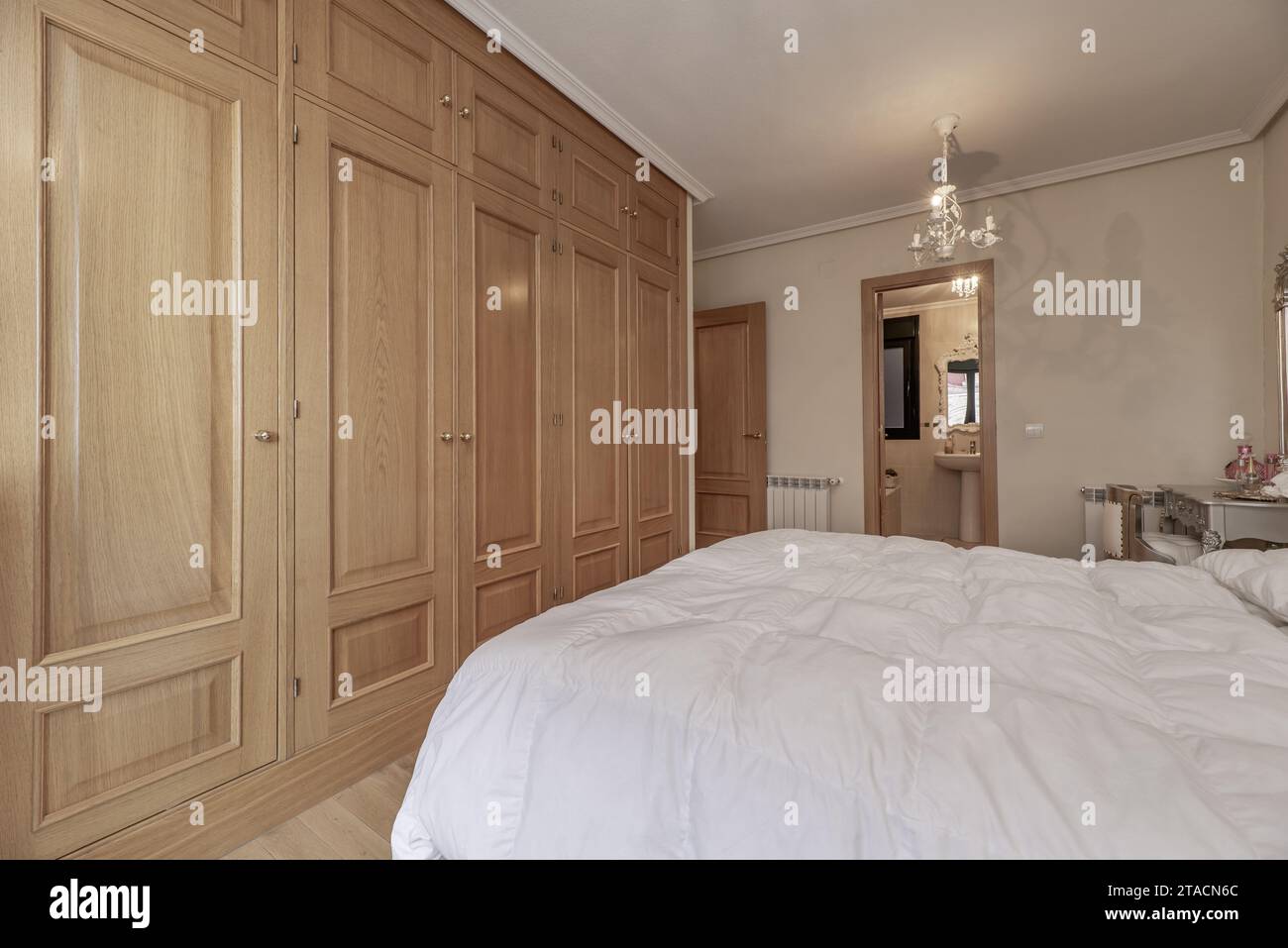 Large built-in wardrobe in the bedroom with oak wood doors, double bed Stock Photo