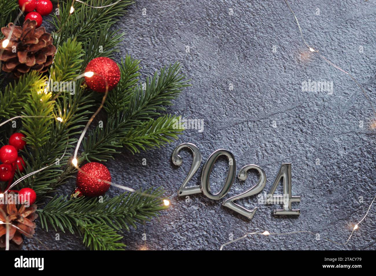 Happy New Year 2024, gray background with fir branch and Christmas balls and glowing garland on a gray background. New Year card, empty space. Christm Stock Photo