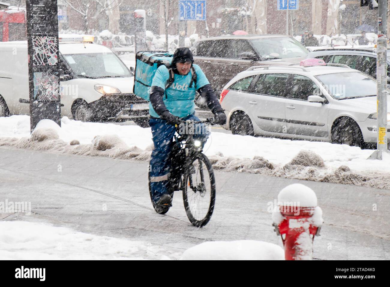 Belgrade, Serbia - January 11, 2022: Winter city traffic in heavy snow storm, and one Wolt delivery courier riding a bicycle on city sidewalk Stock Photo