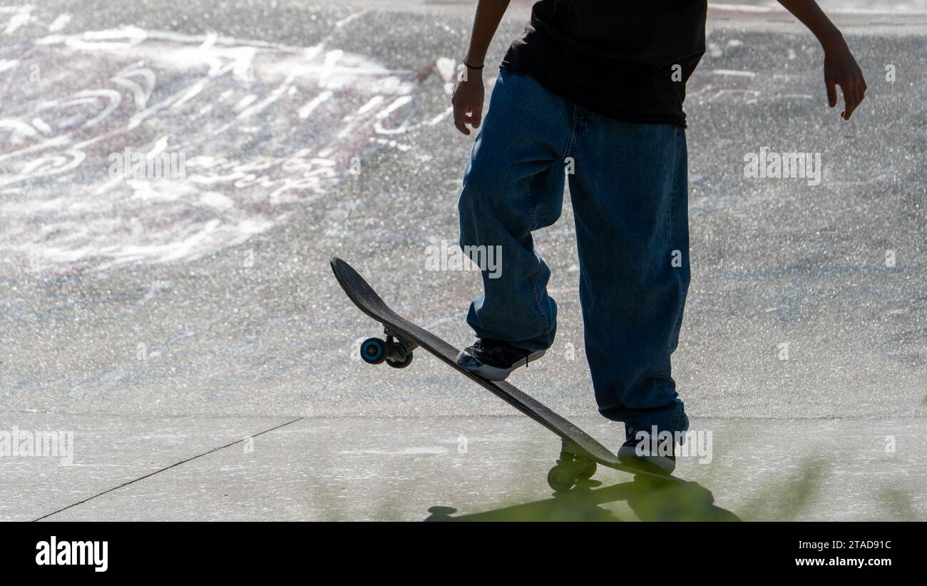 A skateboarder is pictured standing atop their skateboard, looking away