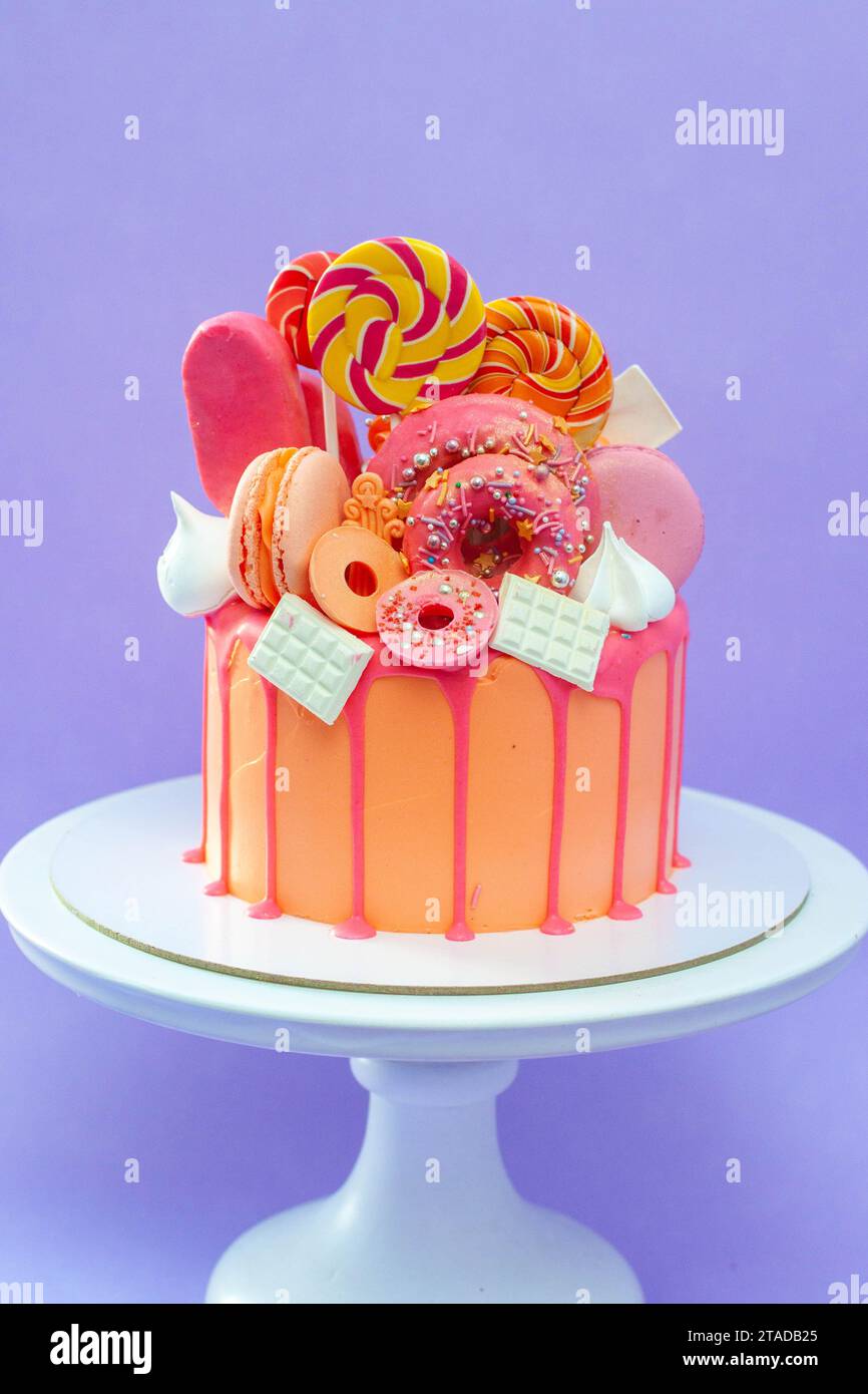 Tasty orange cake with sweets on plain purple background Stock Photo