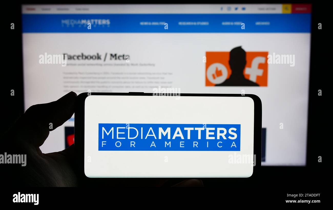 Person holding mobile phone with logo of US watchdog group Media Matters for America (MMfA) in front of webpage. Focus on phone display. Stock Photo