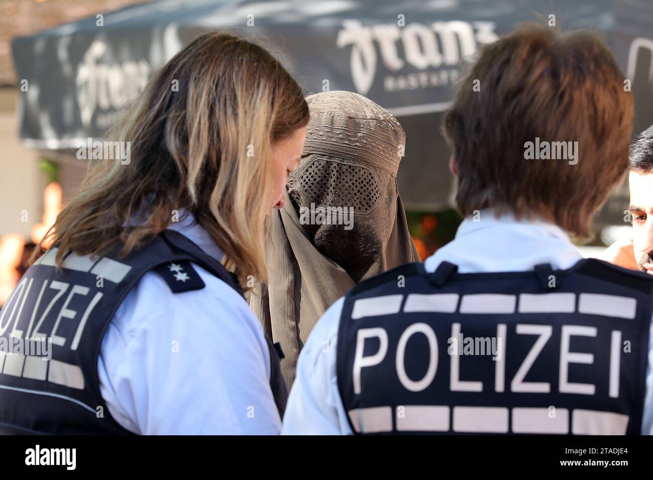 02.09.2023, Iffezheim, Baden-Wuerttemberg, GER - Polizisten stehen vor einer verschleierten Frau. Alltag, Araberin, arabisch, asiatisch, aussen, Aussenaufnahme, Baden-Wuerttemberg, Beamte, Beruf, Berufswelt, deutsch, Deutschland, Einsatz, Europa, europaeisch, Frauen, Gesellschaft, Iffezheim, Islam, Kaukasierin, kaukasisch, Kontrolle, kontrollieren, Menschen, Niqab, Oeffentlicher Dienst, Ordnung, Ordnungshueter, Personen, Personenschutz, Polizei, Polizisten, QF, Querformat, Sicherheit, Sicherheitsbeamte, Streife, verhuellt, Verhuellung, Vermummungsverbot, verschleiert, Verschleierung, Westeurop Stock Photo