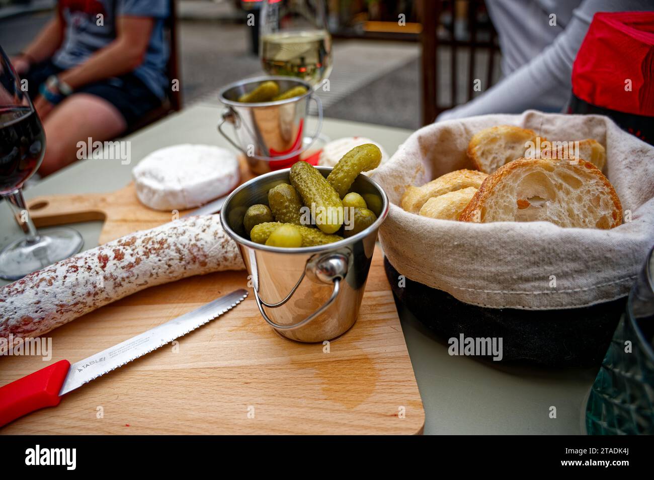 Small green pickles on a rustic charcuterie and cheese spread on wooden board, featuring the iconic Swiss mini red knives. Stock Photo