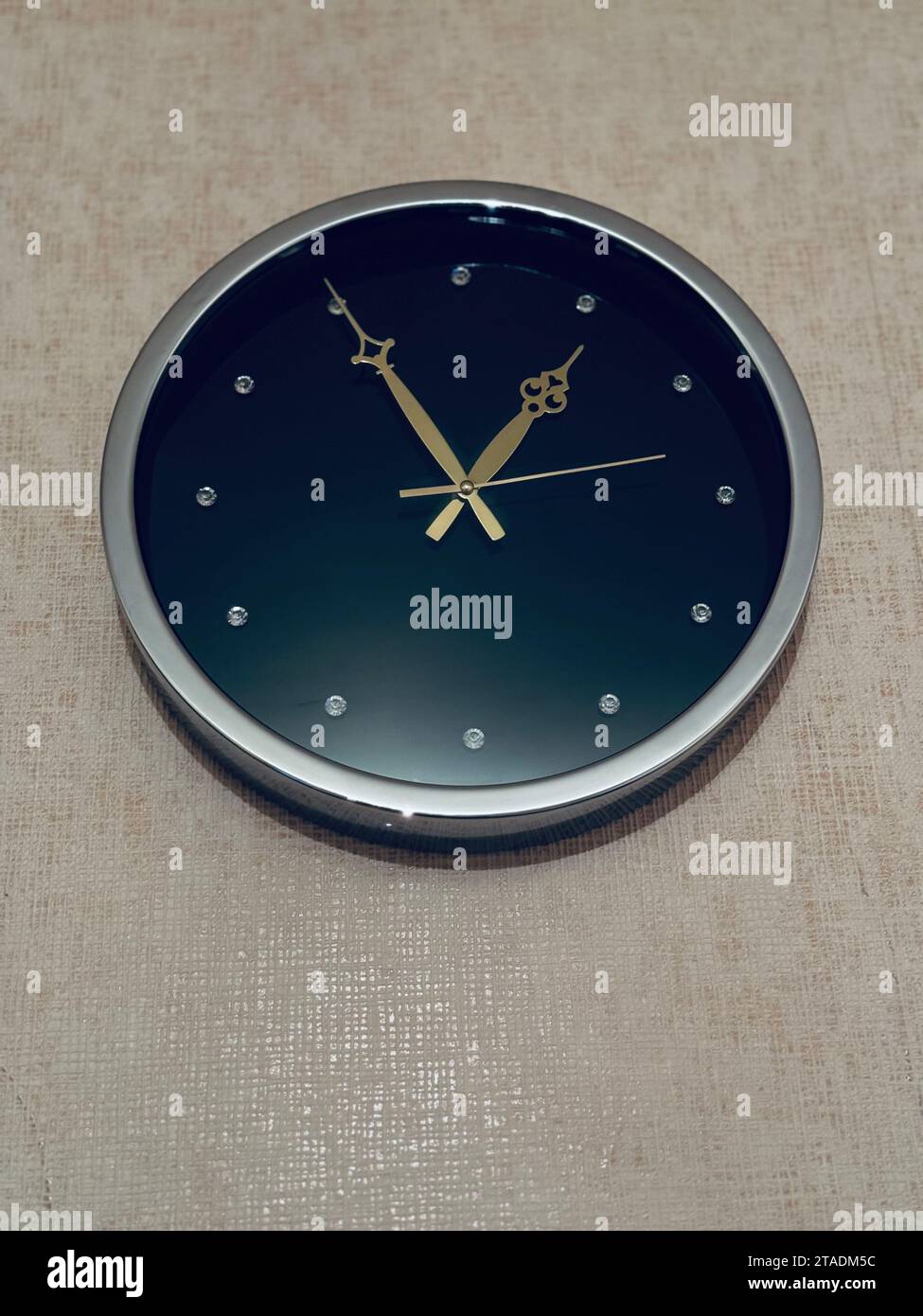 A black and gold wall clock hangs on a tan wall background Stock Photo ...