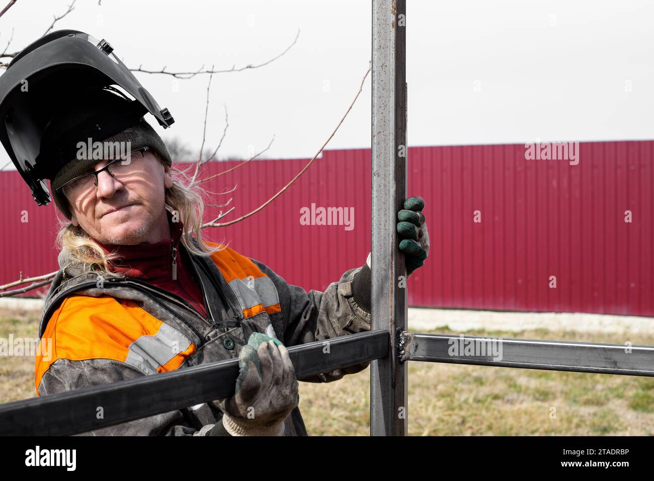 A welder installs an iron frame for construction. Welding metal profiles. Stock Photo