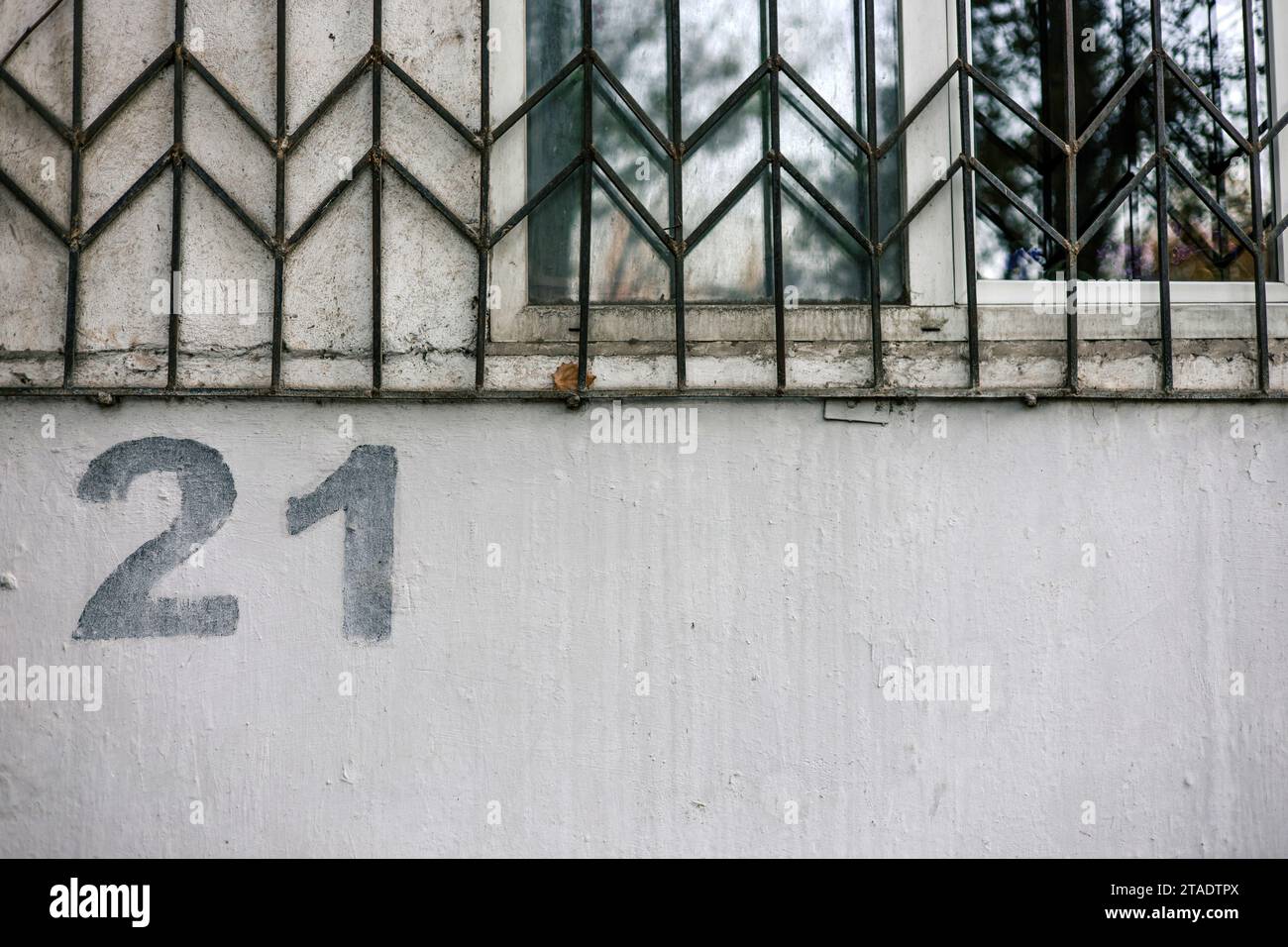 House numbering. The number 21 twenty one is painted using a stencil on a gray wall below a window with bars Stock Photo