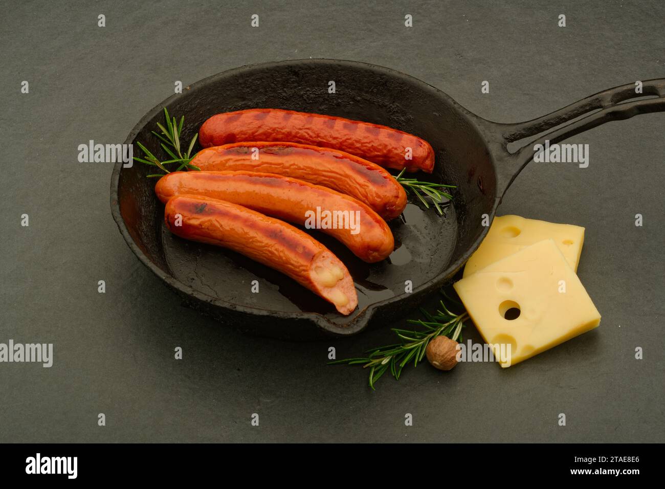German sausages being cooked. With cheese and rosemary garnish. One sausage with cheese filling. Stock Photo