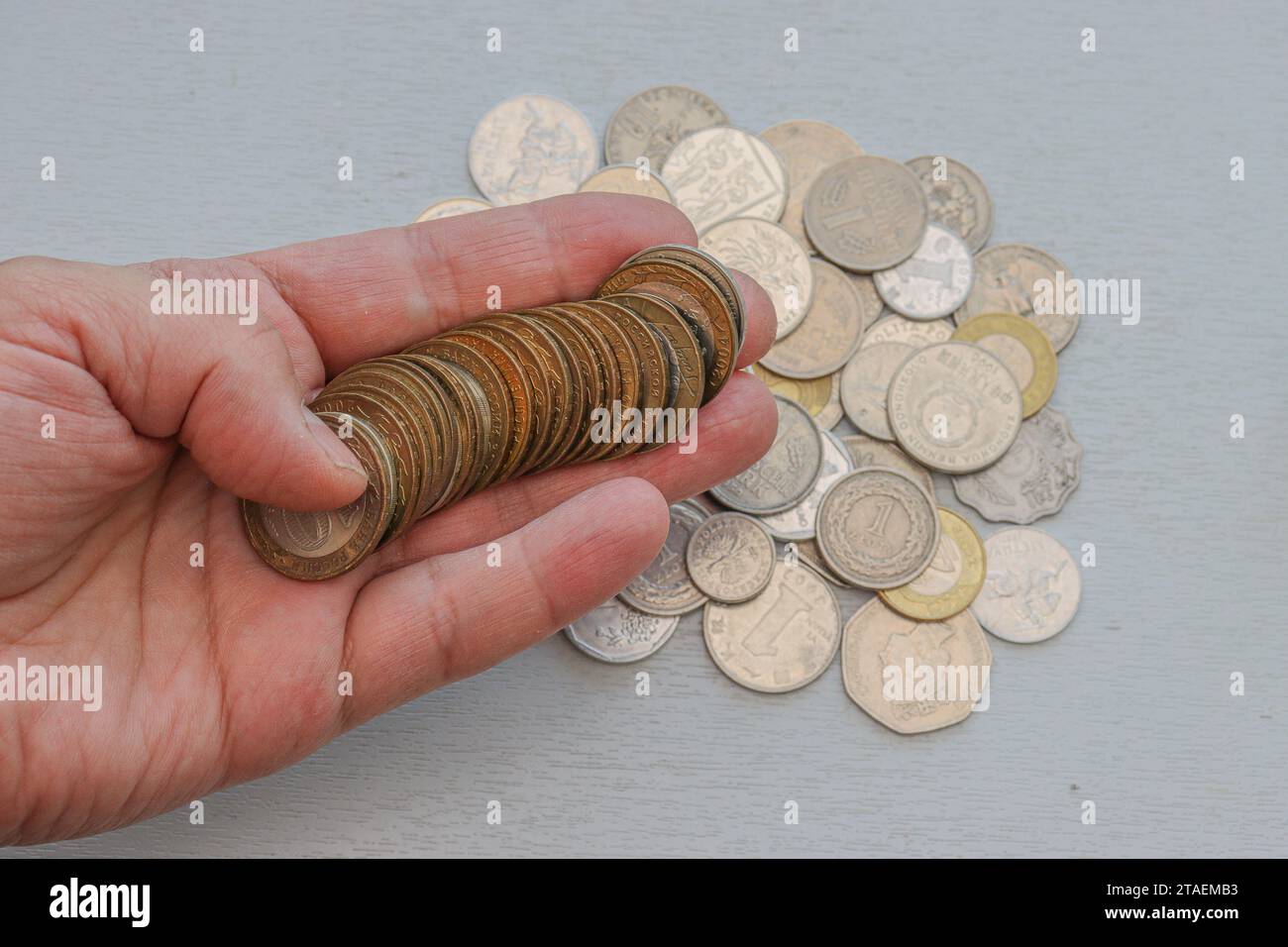 The left male hand holds bimital coins on a light gray background and other various coins in the palm. Stock Photo