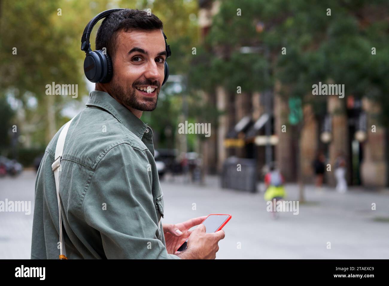 Portrait of a young man walking outside in the street, using phone to listen music, turns to camera. Stock Photo