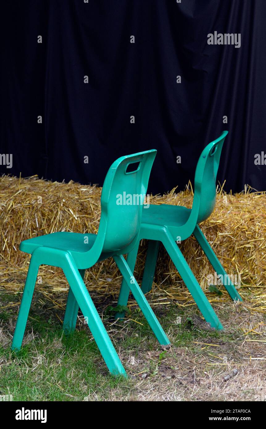 two green plastic garden chairs in front of straw bales at rural