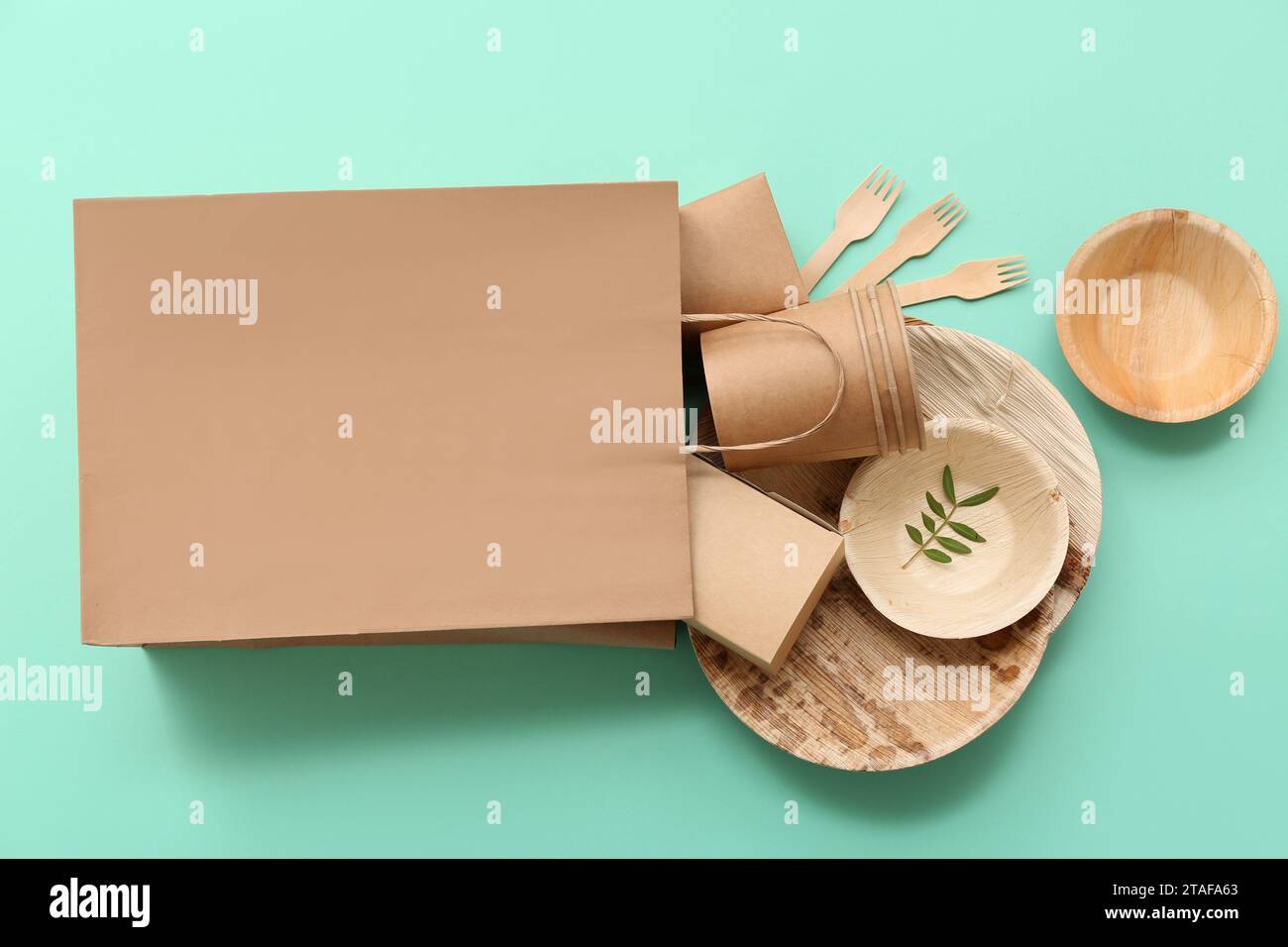 Paper bag with disposable eco tableware on turquoise background Stock Photo