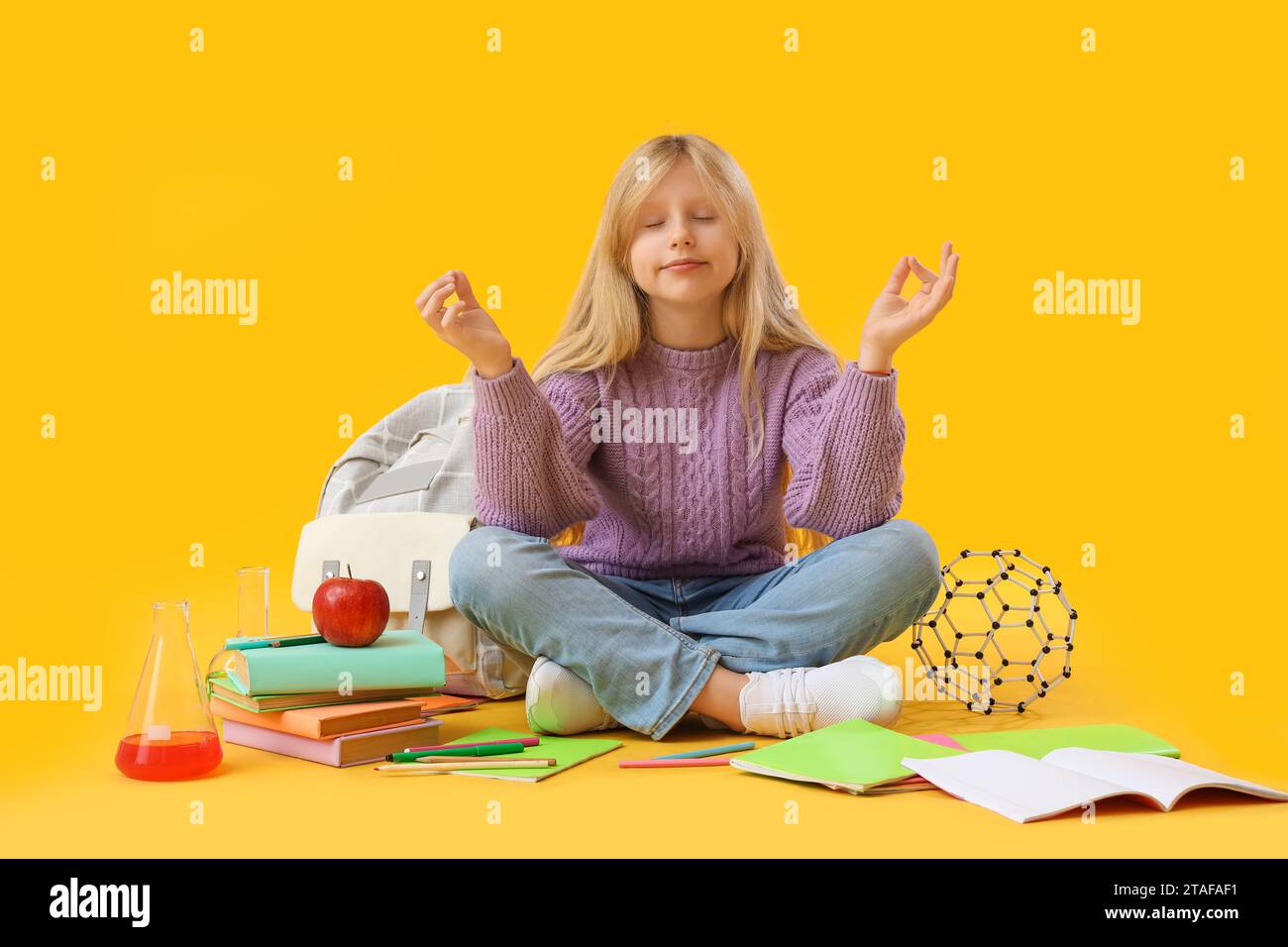 Little schoolgirl with backpack and copybooks meditating on yellow background Stock Photo