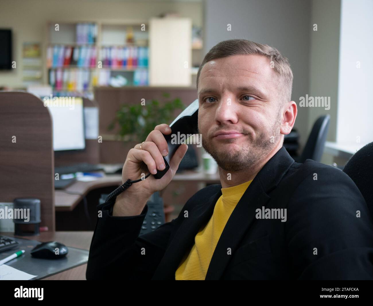 Person is working too hard, his face displays sign of exhaustion, selective focus. Midlife man sitting in the office and talking on the phone Stock Photo