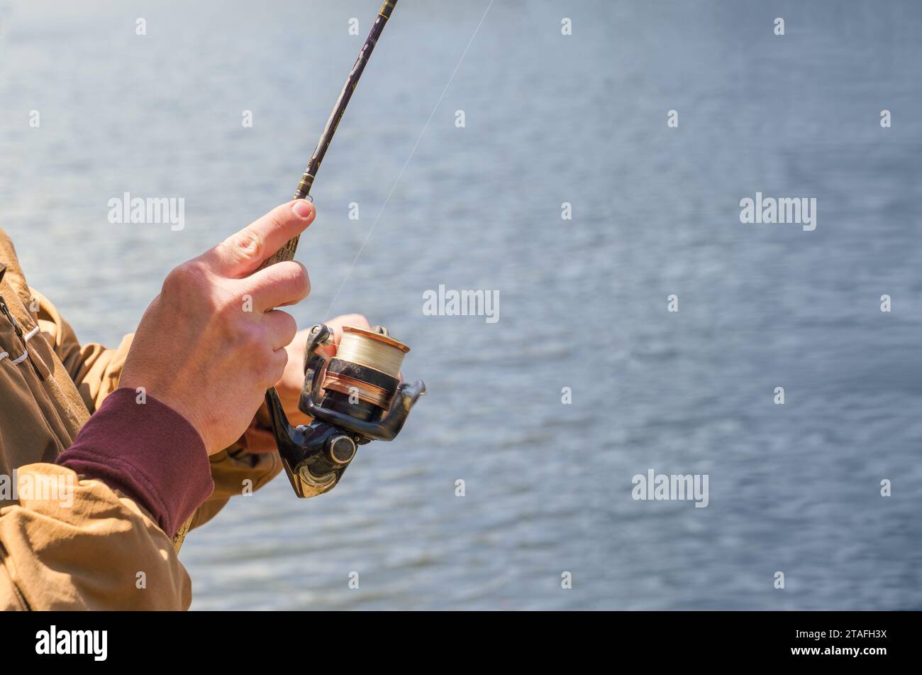 Close-up of a man reeling in with a fishing reel at a lake. Room for copy space. Stock Photo