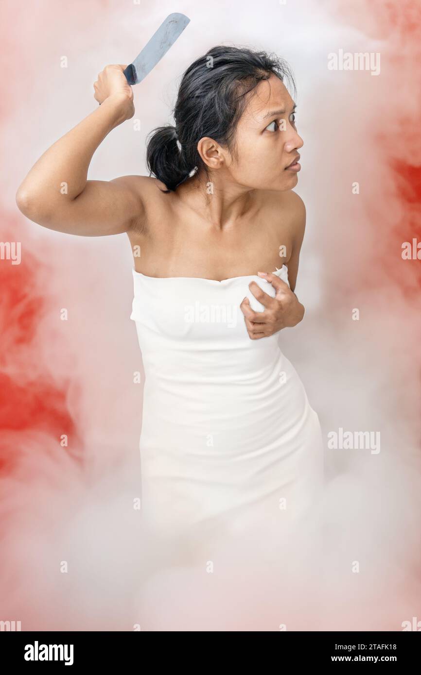 A young woman standing in white smoke is armed with a knife Stock Photo