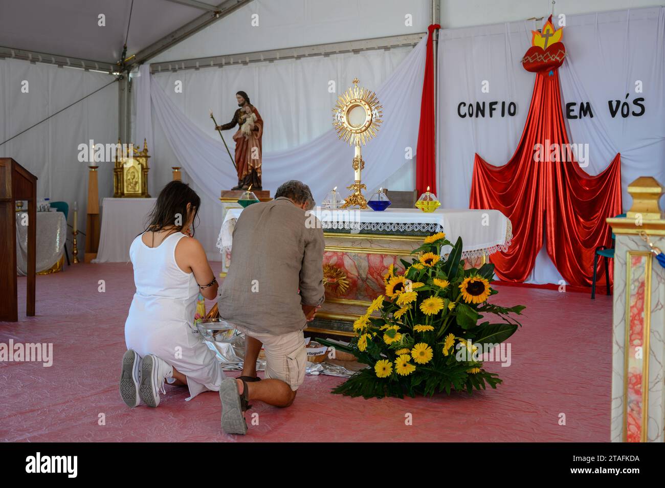 A middle-aged couple kneeling in adoration of the Blessed Sacrament. A tent at the Sanctuary of Christ the King in Lisbon, Portugal during WYD 2023. Stock Photo