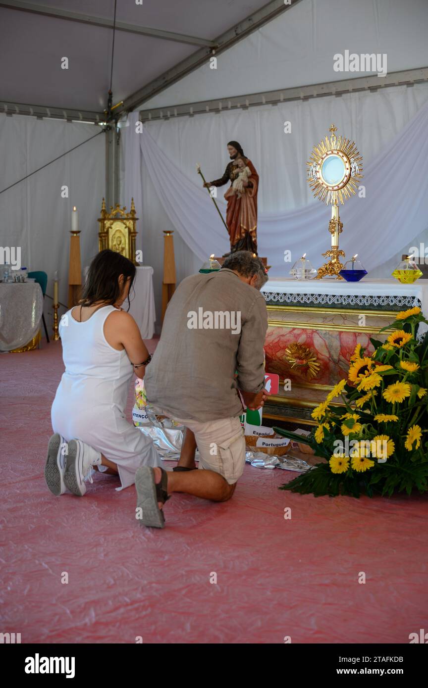 A middle-aged couple kneeling in adoration of the Blessed Sacrament. A tent at the Sanctuary of Christ the King in Lisbon, Portugal during WYD 2023. Stock Photo