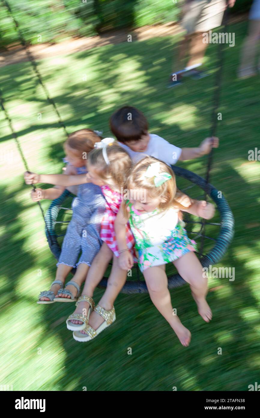 Group of kids ride together on a round rope swing in the backyard, Miami, Florida, USA Stock Photo
