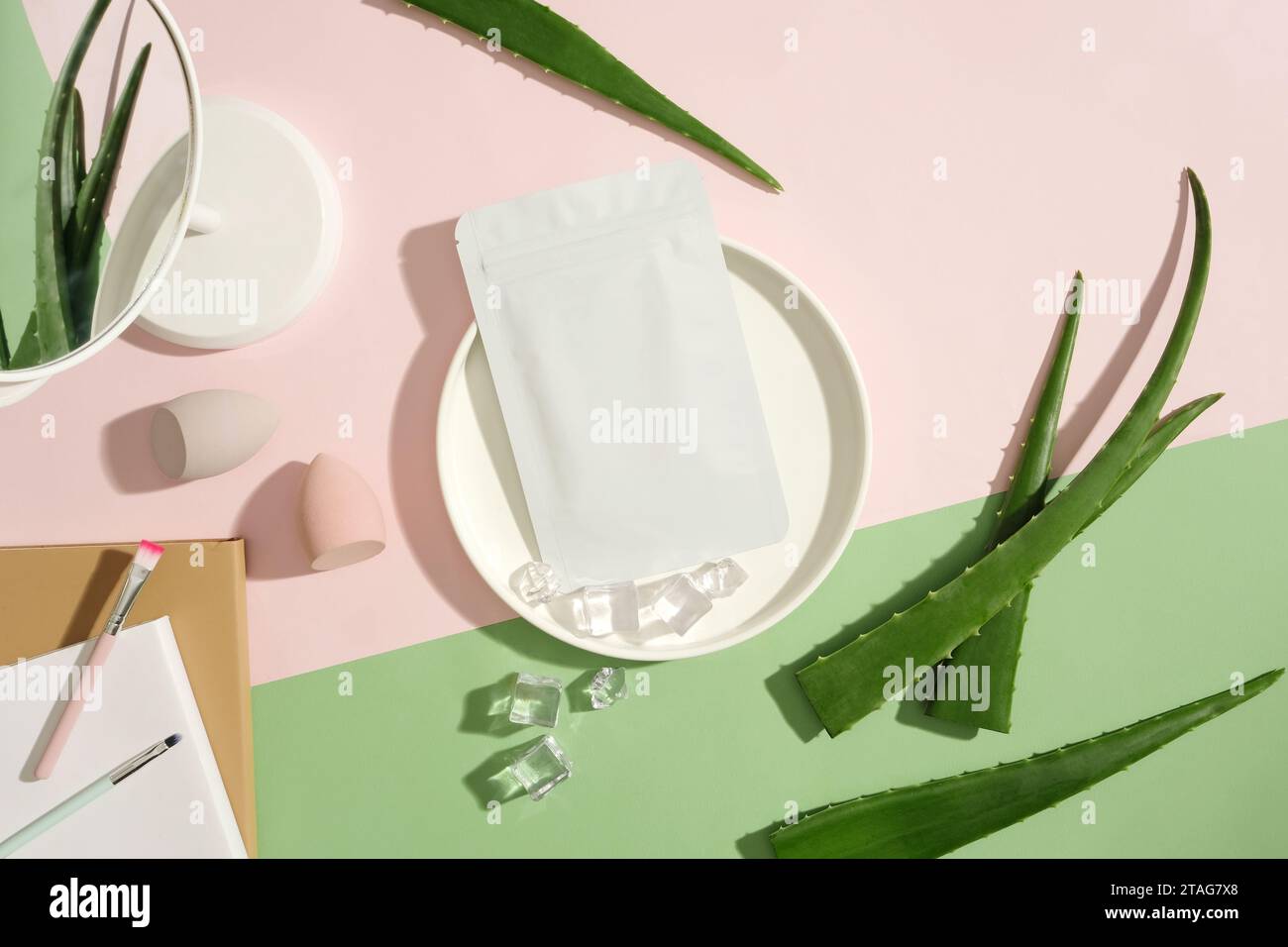 Top view of the unbranded mask placed on a ceramic plate with ice, surrounded by props and fresh aloe vera on a color-coordinated background. Skin car Stock Photo