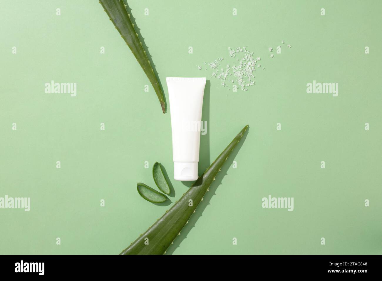 White salt is sprinkled next to an unlabeled tube of facial cleanser and fresh aloe vera leaves on a minimalist background. Aloe vera contains many nu Stock Photo