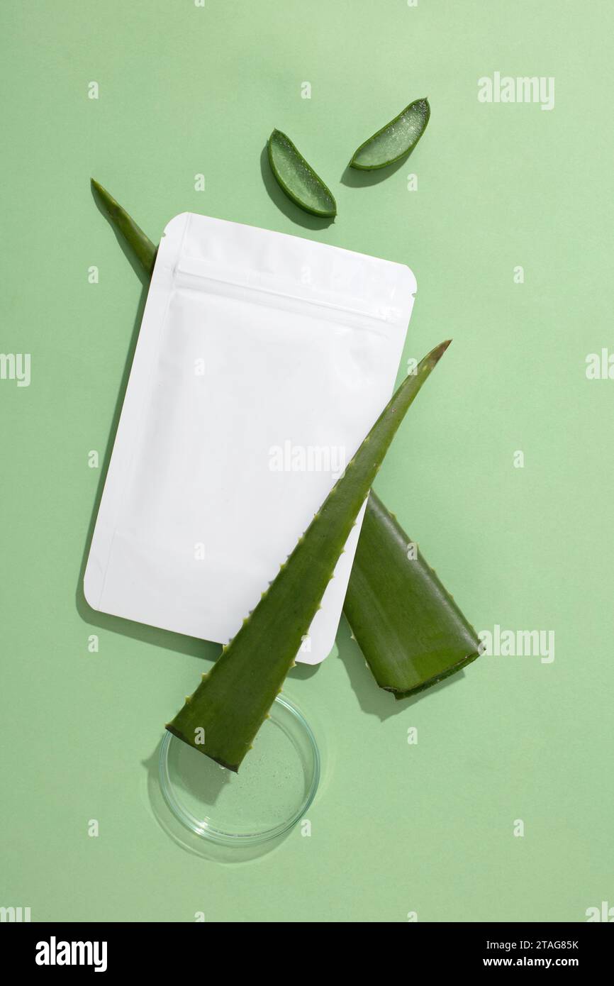 A non-branded mask sheet rests on a fresh aloe vera leaf, beside a clear petri dish, set against a pastel background-a cosmetic brand mockup. Copy spa Stock Photo