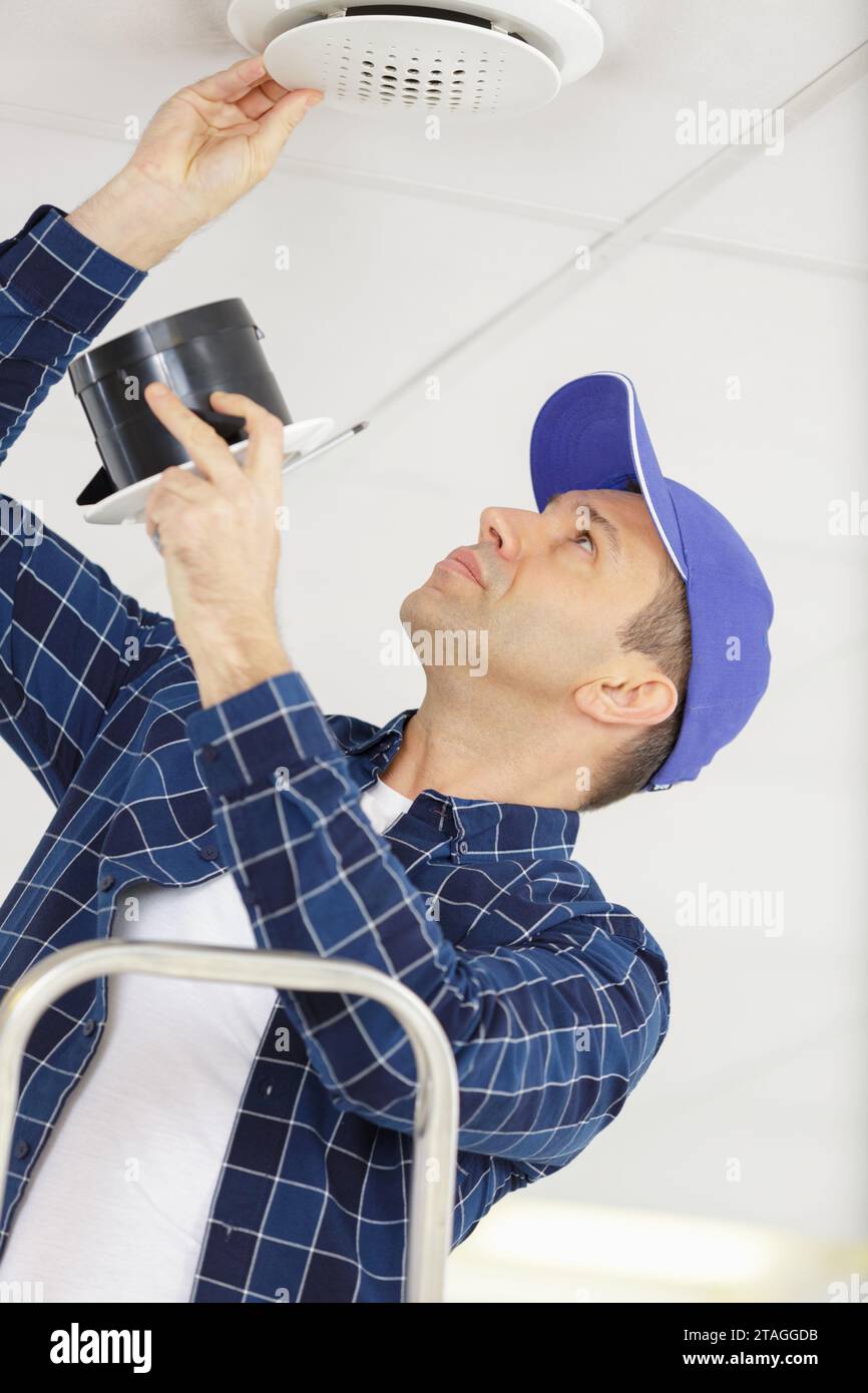 young electrician installing fire alarm unit on ceiling Stock Photo