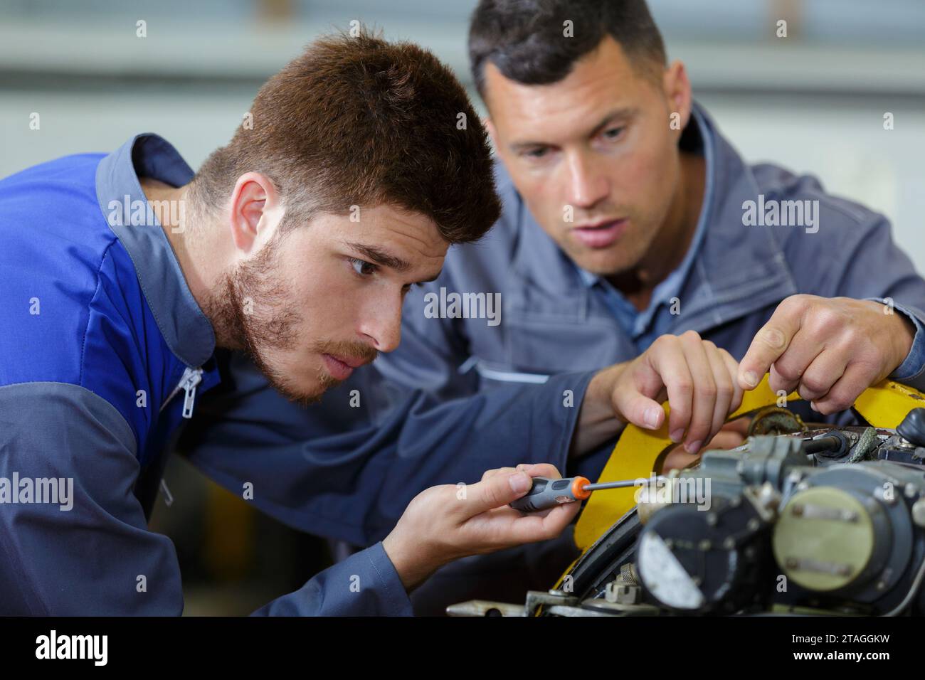 male apprentice engineer using screwdriver under supervisors guidance ...