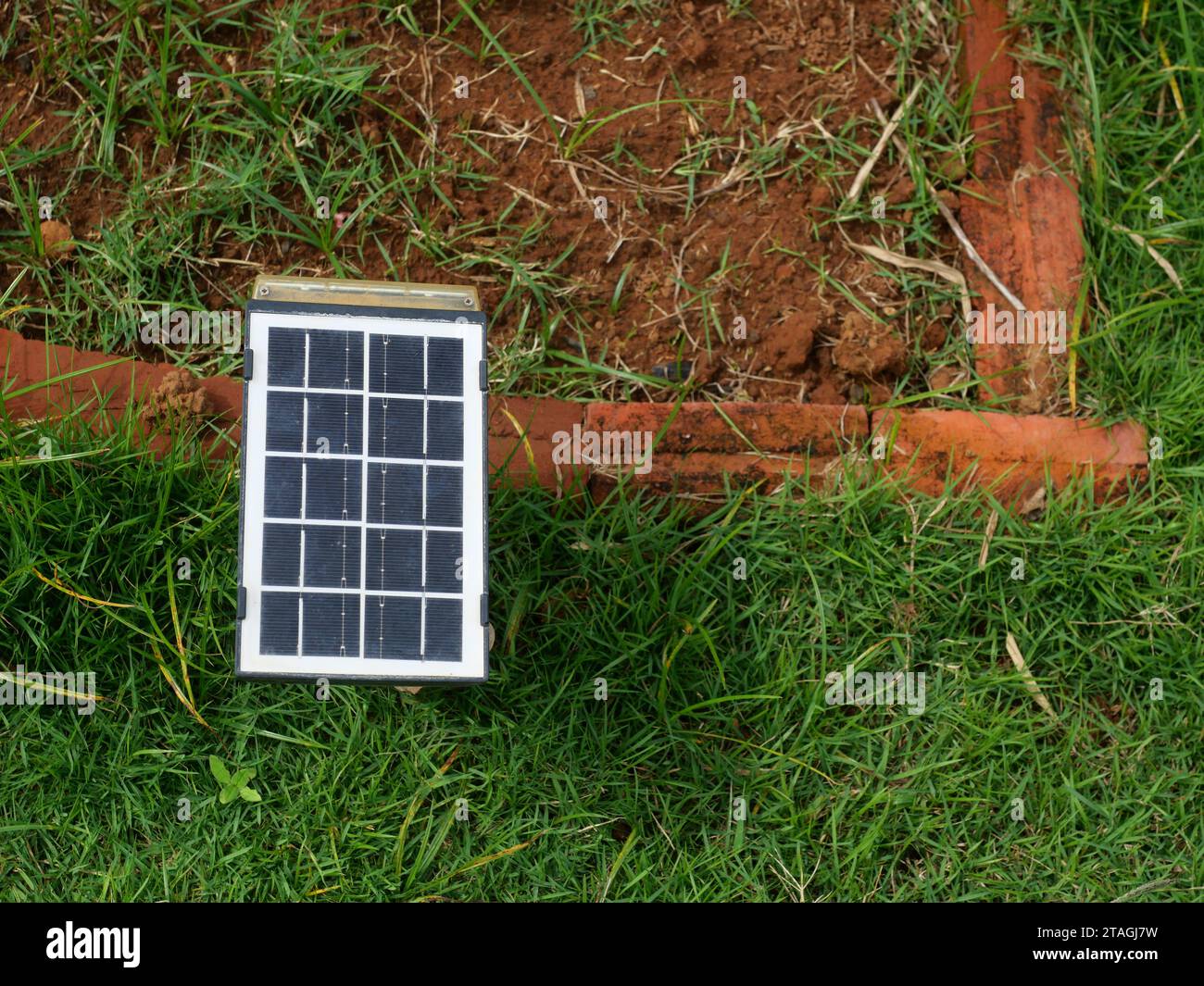 Small portable solar cell panel on the lawn with dirt land and red brick in background, Clean energy for electricity generation in the home Stock Photo