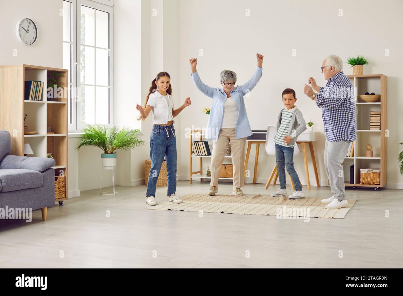 Happy cheerful grandparents having fun with grandchildren dancing at home. Stock Photo