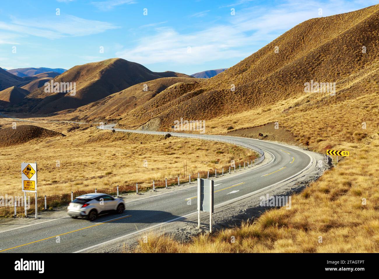The road through the Lindis Pass in the South Island of New Zealand. Snow tussock grows on the mountains Stock Photo