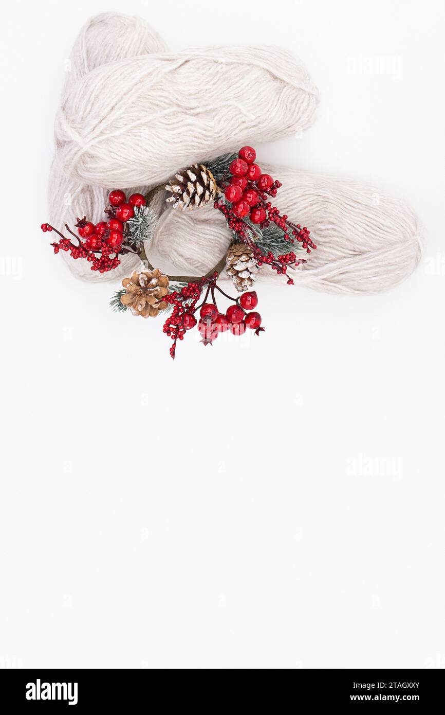 Gray wool skeins or wool yarn with a branch of red berries and pine cones on white background. Handmade, knitting, hobby. Copy space Stock Photo