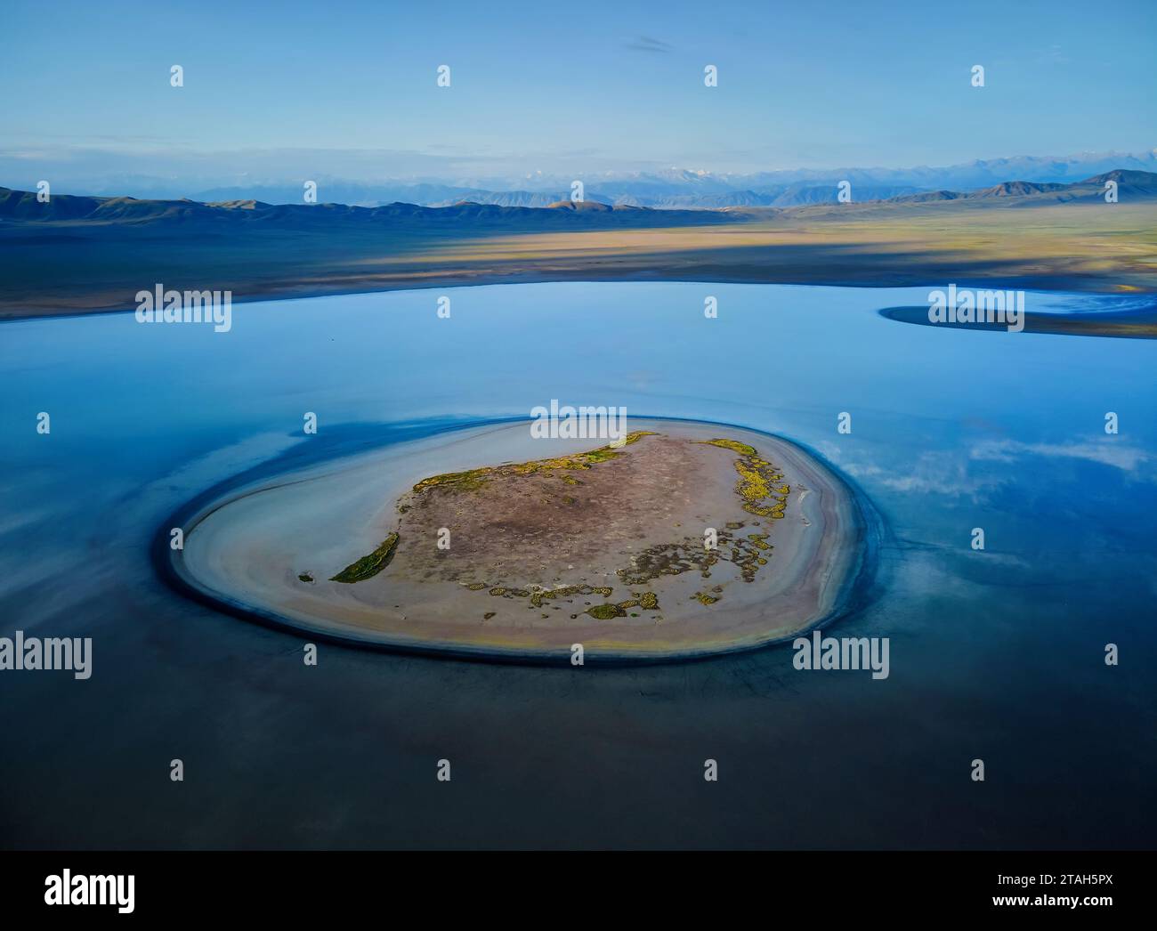 Aerial drone shot of beautiful scenery of Small Island at blue mountain lake TuzKol with green hills at twilight glow in Mountains of Kazakhstan. Stock Photo