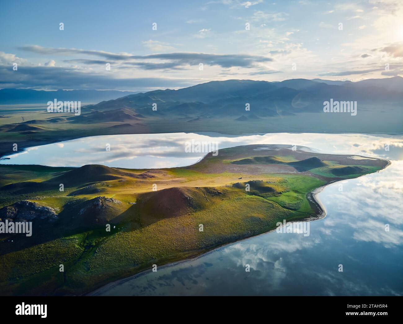 Aerial drone shot of beautiful scenery of blue mountain lake TuzKol with green hills at sunset light glow in Mountains of Kazakhstan. Stock Photo