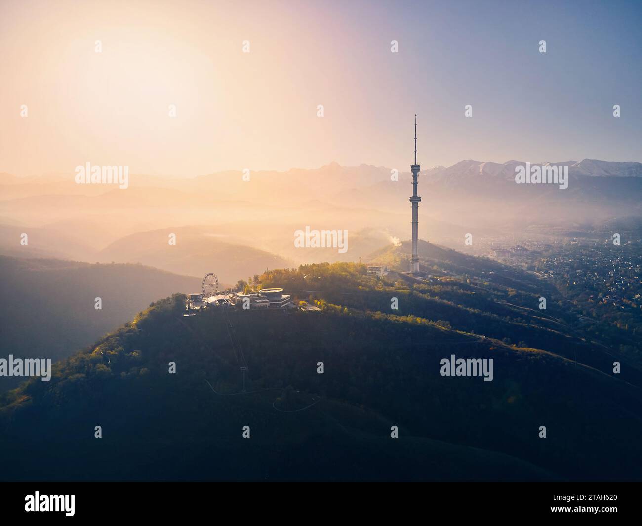 Aerial drone shot of symbol Almaty city high TV tower and park at Koktobe hill against snow mountains at sunrise in Kazakhstan Stock Photo