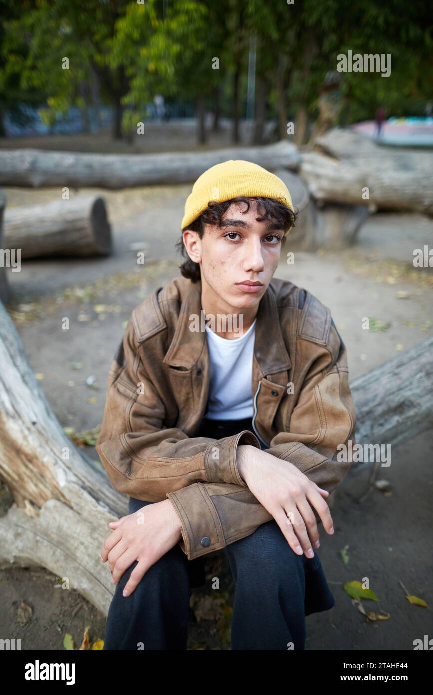portrait of a young man with acne sitting on a log in the park Stock Photo