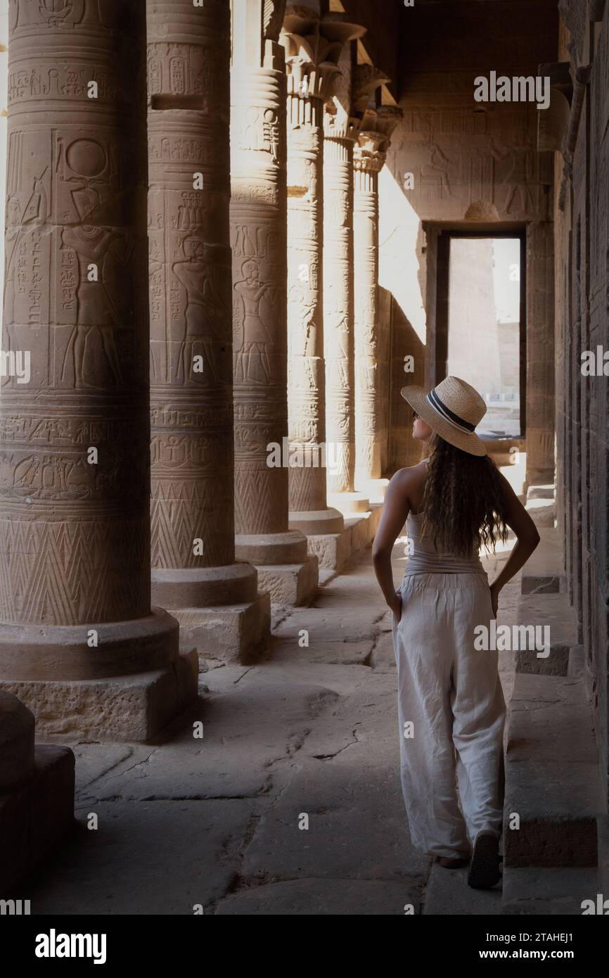One woman wearing hat, walking next to columns of Egyptian temple Stock Photo